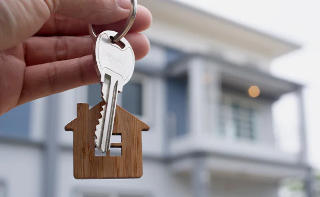 Hand holding keys with house keyrings in front of house
